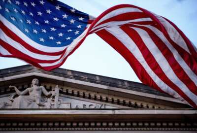 FILE - An American flag flies outside the Department of Justice in Washington, March 22, 2019. The Justice Department says three Iranian citizens have been charged in the United States with cyberattacks that targeted power companies, local governments and small businesses and nonprofits, including a domestic violence shelter. (AP Photo/Andrew Harnik, File)