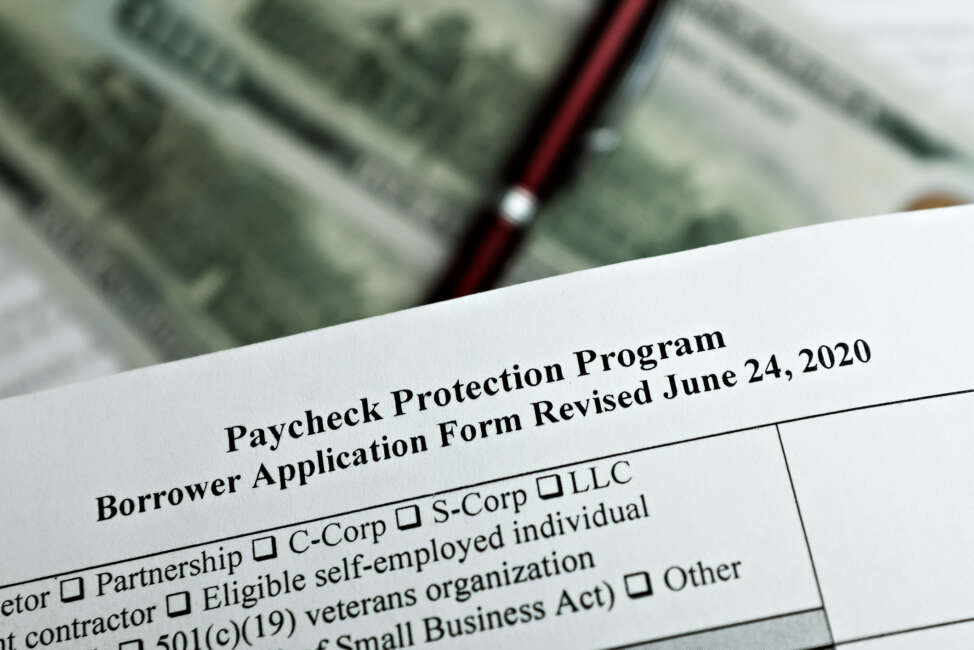 selective focus photo of paycheck protection program borrower application form revised, on a background of dollar bills and a pen