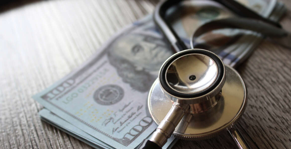 Stethoscope and money on wooden table representing health care, FEHB plans.