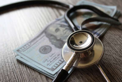 Stethoscope and money on wooden table representing health care, FEHB plans.