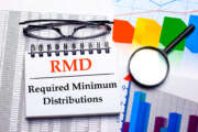 Glasses, magnifier, color charts and a white notepad with text RMD Required minimum Distributions on the desktop. Business concept. View from above