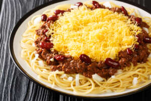 Cincinnati chili spaghetti with red beans, cheese and onion close up in the plate on the black wooden background. 