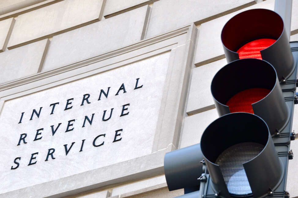 IRS sign with a traffic signal in the foreground indicating a red light.