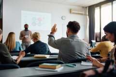 Rear view of man raising arm to ask a question during a presentation in lecture hall.