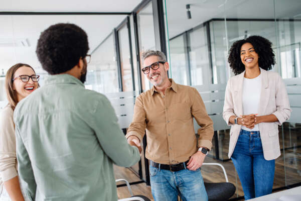 A friendly office environment is depicted where a team greets each other and shaking hands